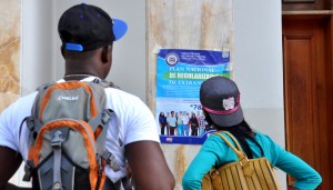 Dos haitianos frente a la Gobernación de Santiago leen un cartel con los requisitos para iniciar el proceso de regularización.